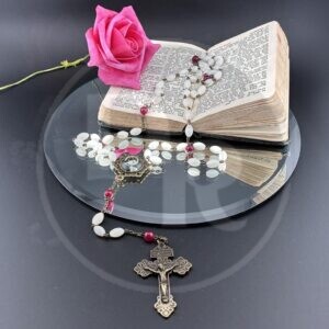 A catholic rosary with elongated white beads and dark red beads and finished with antiqued bronze wire, crucifix and centrepiece which features a blakc and white photo of Saint Maria Goretti.