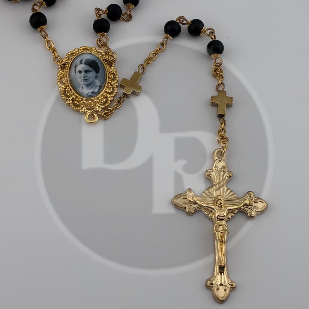 A black rosary for Catholics with a golden crucifix and centrepiece. The centrepiece has a small black and white photo of Saint Edith Stein